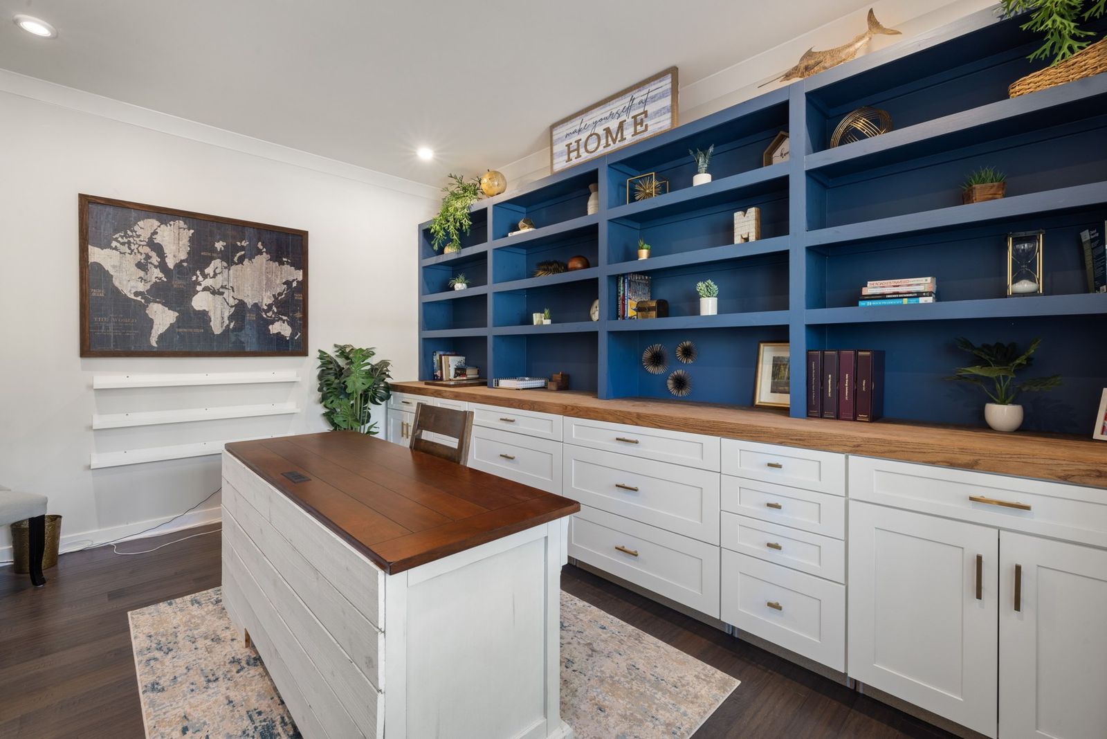 Home office with a long run of white lower cabinets and navy open bookshelves (example style photo)